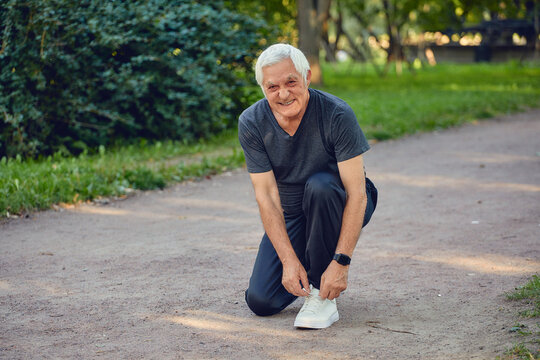 Elderly man in sportive wear ties shoelaces ready for jogging