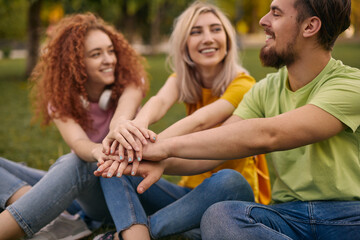 Cheerful young friends stacking hands and smiling in park