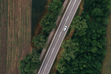 Top view of straight asphalt highway through countryside landscape in summer with car driving along the road, drone pov
