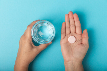 Woman's hands hold vitamin pill and glass of water on blue background.Ready to take medicine for...