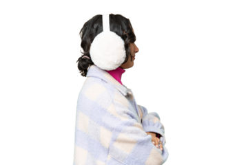 Young Argentinian woman wearing winter muffs over isolated background in lateral position