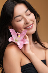 Content smiling Asian woman with closed eyes and lily flower in studio