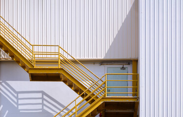 Yellow fire escape on white corrugated steel wall outside of industrial building