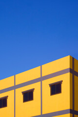 Street minimal exterior architecture background. Glass windows on colorful yellow and purple house building wall against blue clear sky background in vertical frame