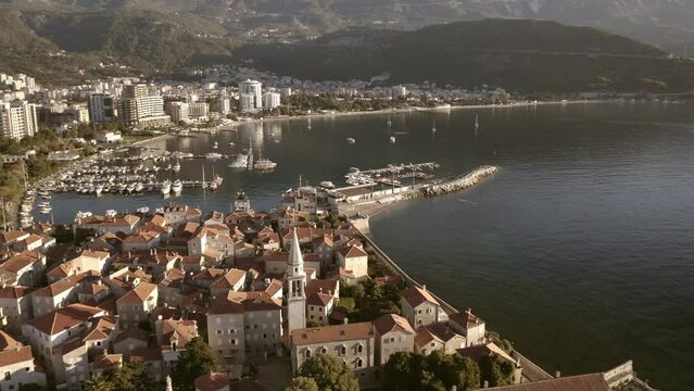 Drone flight over the city of Budva in Montenegro, old town, houses with red roofs and marina with boats.