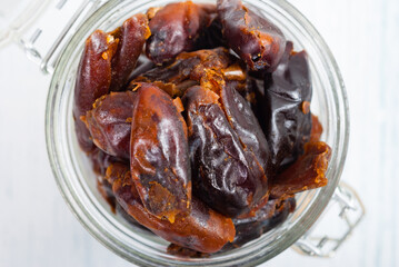 sun dried date fruits at glass jar, white wooden table background