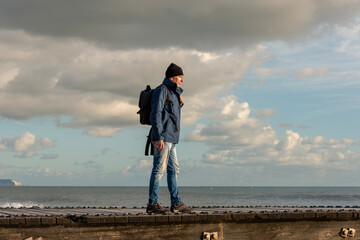Man with backpack by the ocean, autumn, winter walk.