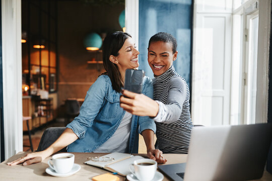 Smiling female entrepreneurs taking selfies while working in a cafe