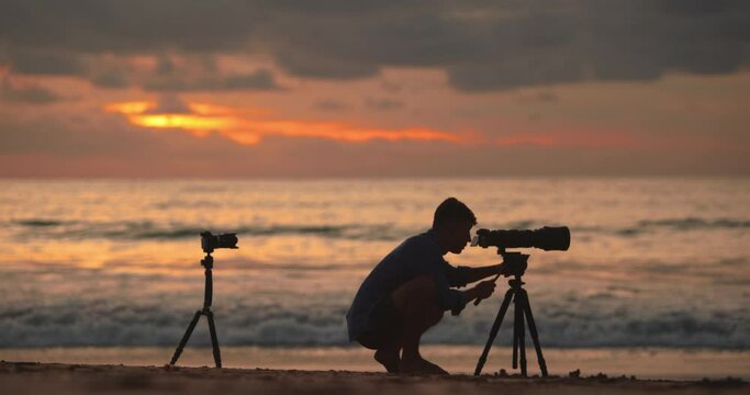 Silhouette of a man photographer with professional cameras and long lens and tripod photographs a beautiful sunset 4K