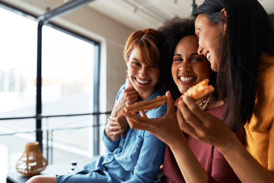 Smiling girlfriends eating pizza