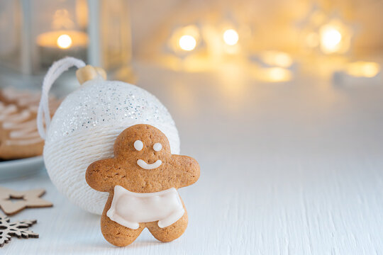 Homemade spicy sweet brown gingerbread man cookie or biscuit  baked with ginger and cinnamon spices with white christmas bauble on wooden table with garland and candle lights. Image with copy space