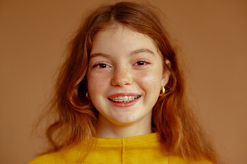 Happy smiling redhead freckled girl with dental retainer. Close up portrait. Beige background,...