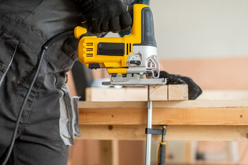 Close-up of a man cutting a wooden plank with an electric jigsaw in a workshop.