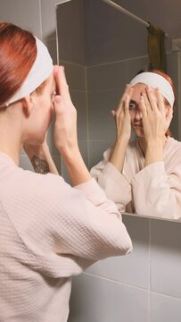 Beauty Day. Woman doing her daily skincare routine in bathroom and mirror gently puts cream on her face and spears it until it is absorbed. Concept of beauty, self-care, cosmetics, youth.
