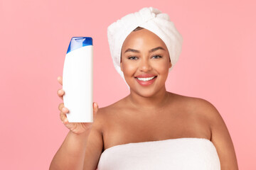 Happy african american chubby woman showing blank shampoo bottle, advertising body and haircare...