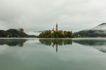 Aerial view of Island in Bled Lake, with Bled city in background. Church and other buildings in the...