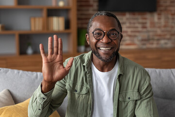 Headshot of smiling middle aged african american male waving hand at camera, greets, says hi, has...