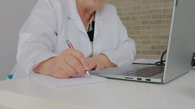 Close up senior doctor hands taking notes from a healthcare letter send by email. Female nurse studies online. Health care and insurance concept.