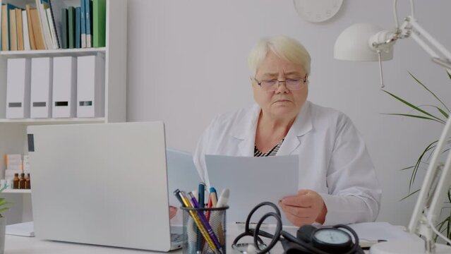 Female doctor analysing paperboard report tired taking her glasses of. Tired docor needs a rest. Medicare concept.