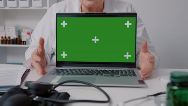 Close up of green screen laptop mockup doctor explaining in white gown while sitting in health clinic. Doctorate having online conference.
