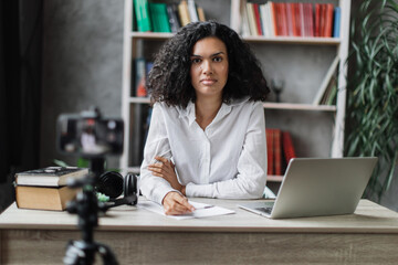 Beautiful multinational woman in white shirt talking while looking at and recording video on modern...