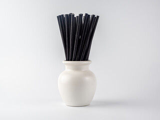 white vase pot containing black bio degradeable bamboo cocktail straws on a white background