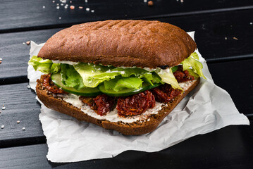 Sandwich with sun-dried tomatoes, lettuce, cucumber and mayonnaise on a rye bun.