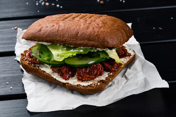 Fast food sandwich with sun-dried tomatoes, lettuce, cucumber and mayonnaise on a rye bun.