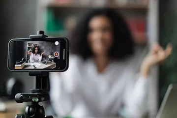  Blurred relaxed young woman in casual wear sitting on workplace with modern laptop and meditating with closed eyes during recording video blog. Focus on modern smartphone fixed on tripod. © sofiko14