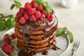 Chocolate Pancakes. Pancakes with fresh raspberry with chocolate glaze or toppings in gray bowl on light gray table background. Homemade classic american pancakes. Page for magazine concept.