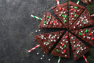Chocolate brownies Christmas tree with chocolate icing and festive sprinkles on stone table. Christmas food ideas sweet homemade Christmas holidays pastry concept. Holiday cooking concept. Top view.