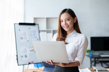 Beautiful Asian business woman standing holding a laptop in the office