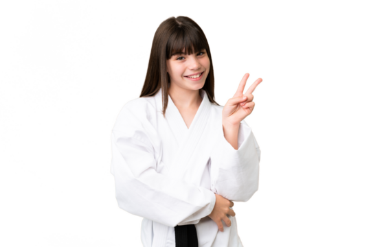 Little Caucasian girl doing karate over isolated background smiling and showing victory sign