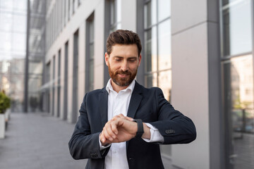 Smiling confident young european guy boss with beard in suit look time at clock, waiting for meeting