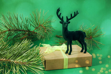 Christmas card: toy deer on a wrapped gift, pine branches on a green background, bokeh, side view, space for text