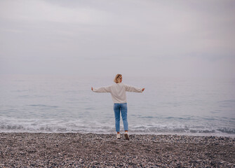 happy woman stands on the sea sand and shows her hand in the sky. the subject is blurred