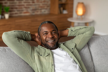 Cheerful middle aged african american man resting on sofa, enjoying free time alone, silence and...