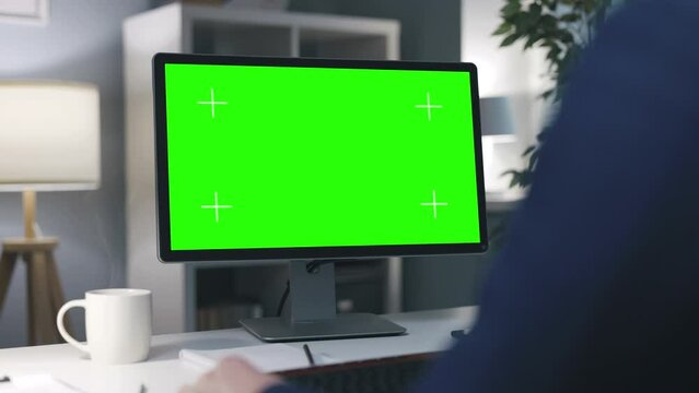 Businessman having video conference on blank chromakey screen of computer, evening office workplace with cup of steaming coffee