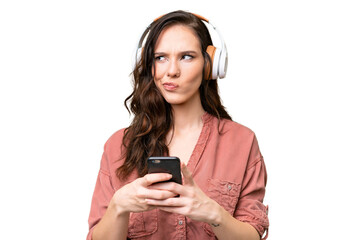 Young caucasian woman over isolated background listening music with a mobile and thinking