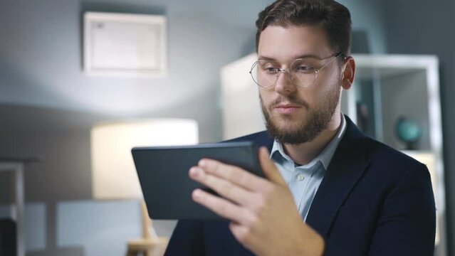Confident young businessman in eyeglasses having video chat using tablet, focused successful freelancer have conference with team, remote conection concept