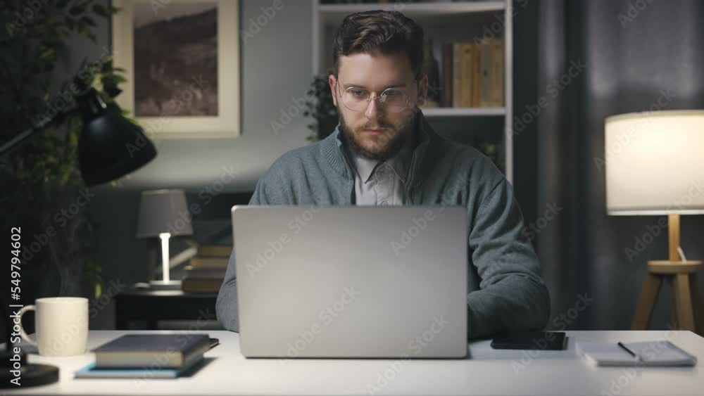 Poster young handsome man using laptop for internet browsing, bearded man in eyeglasses working from home. 