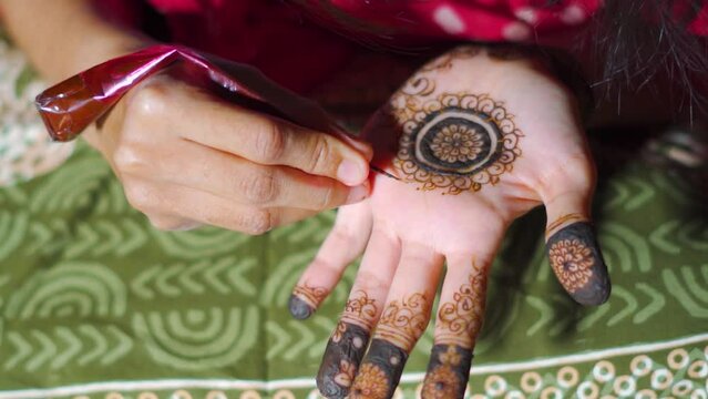 Close up shot of Hindu Indian girl applying Mehndi design in her hand. Indian wedding mehndi ceremony. Heena tattoo on hand of girl.