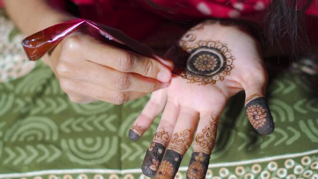Close up shot of Hindu Indian girl applying Mehndi design in her hand. Indian wedding mehndi ceremony. Heena tattoo on hand of girl.