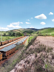 some Train cars empty and others fully loaded with ore. Landscape showing blue sky, mountains and cloud on the background at Itabira Minas Gerais, Brazil.