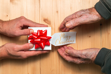 Top view of hands from a young adult giving a Christmas gift to an old man hands with vitiligo over a wooden table