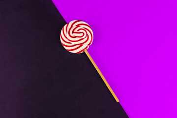 One red and white round candy on a stick on a black and purple background