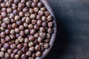 Dry hazelnuts in a ceramic plate on a wooden background. Heap of peeled hazelnuts kernels, top view, copy space for text