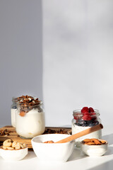 Yoghurts in glass jars with blueberries, raspberries and chia seeds and granola on a wooden board on a white background. The concept of healthy eating. Front view