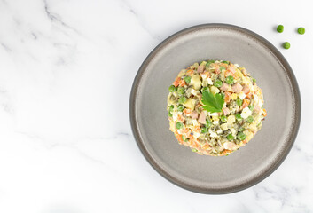 Russian Olivier salad of vegetables, sausage and mayonnaise on a gray plate, white background. Top view, copy space.