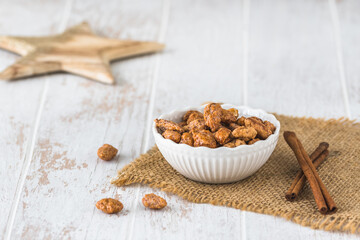 Bowl of sweet candied almonds on white rustic wooden background